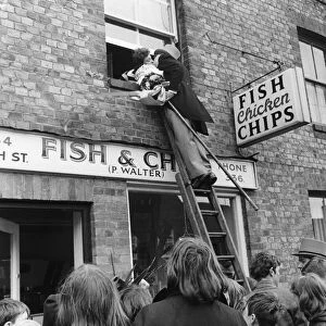 The bridegroom climbs a ladder to kiss his bride at the window above a fish and chip shop