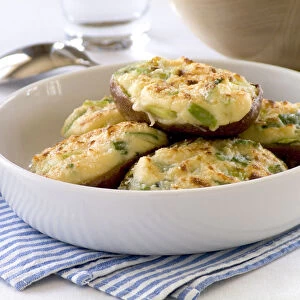 Halved baking potatoes baked with topping of cheese and spring onions credit: Marie-Louise