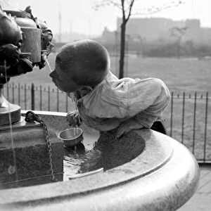 London summer. A little boy drinks water from a fountain. 1933