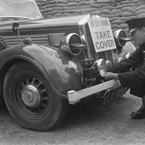 A policeman is fitting an air raid siren along with a warning sign to a police car