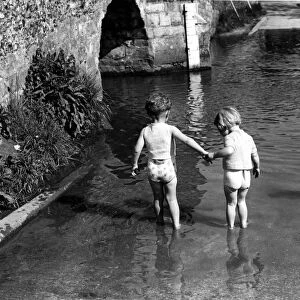 Two small children hold hands as they tentatively paddle deeper. Eynsford, Kent