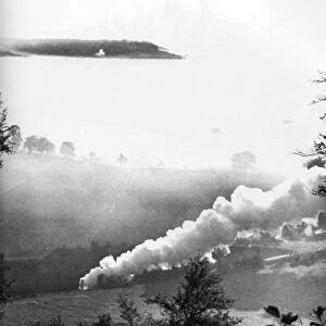 A steam train rattles through a misty valley