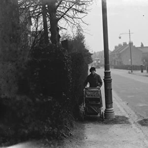 A woman pushes a pram past a street light which is shrouded by branches in Sidcup, Kent