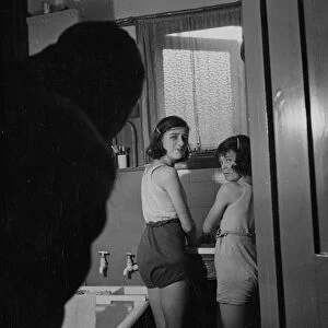 Two young girls in a bathroom, standing by a sink. [no caption, location or date]