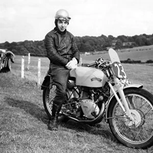 A young John Surtees sitting astride his Vincent motorbike at a race track