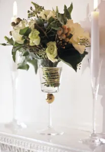 Arrangement of white roses and greenery in tall goblet glass between candles in tall Arrangement of white roses and greenery in tall goblet glass between candles in tall