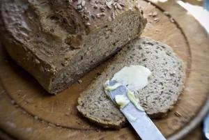 Buttering a slice of bread from a wholegrain, rye and walnut loaf on old wooden board Buttering a slice of bread from a wholegrain, rye and walnut loaf on old wooden board