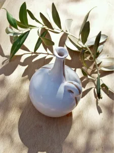 Ceramic oil bottle on tabled dappled in Italian sunshine with branch from olive tree Ceramic oil bottle on tabled dappled in Italian sunshine with branch from olive tree