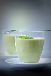 Chilled soup of fresh garden peas and courgettes in small glasses on white saucers Chilled soup of fresh garden peas and courgettes in small glasses on white saucers