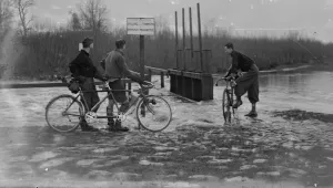 Cyclists look at the high water levels and flooding at the sluice by the river at Cyclists look at the high water levels and flooding at the sluice by the river at