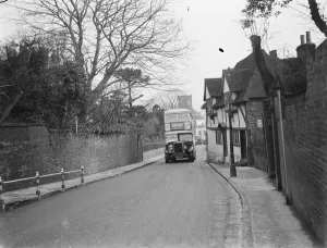 A double decker bus driving past some old cottages on a street in Ashford, Kent A double decker bus driving past some old cottages on a street in Ashford, Kent