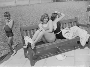 Two girls enjoy the sun in their swimming costumes by the side of a bathing pool Two girls enjoy the sun in their swimming costumes by the side of a bathing pool