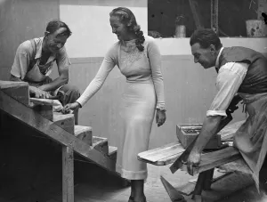 Miss Elmina Humphreys, the radio Queen, holding a nail for one of the workmen building Miss Elmina Humphreys, the radio Queen, holding a nail for one of the workmen building