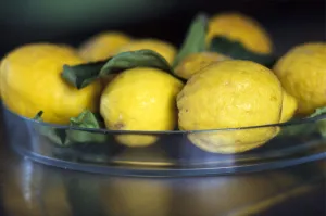 Natural, mediterranean lemons with leaves in glass dish on stainless steel counter Natural, mediterranean lemons with leaves in glass dish on stainless steel counter