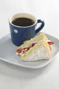 A piece of strawberry sponge cake on a white plate with a small blue and white spotted A piece of strawberry sponge cake on a white plate with a small blue and white spotted