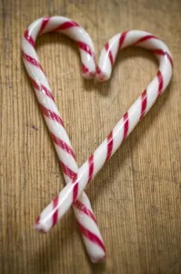 Two red and white striped candy canes on wooden surface crossed to make heart shape Two red and white striped candy canes on wooden surface crossed to make heart shape