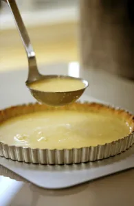 Spooning lemon mixture into pastry case sitting on baking sheet, to minimise spillage Spooning lemon mixture into pastry case sitting on baking sheet, to minimise spillage