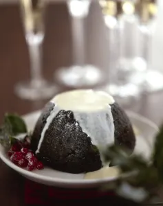 Traditional British Christmas pudding with thin cream or custard poured over Traditional British Christmas pudding with thin cream or custard poured over