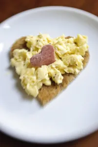 Valentines day breakfast of scrambled eggs on heart shaped toast with slice of salami Valentines day breakfast of scrambled eggs on heart shaped toast with slice of salami