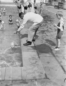 A young girl is taught how to swim with the use of a rope round her waste to keep A young girl is taught how to swim with the use of a rope round her waste to keep
