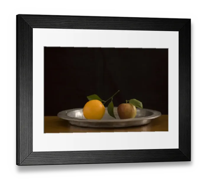 Framed Print : Apple and orange with leaves on pewter charger with black background credit: Marie-Louise