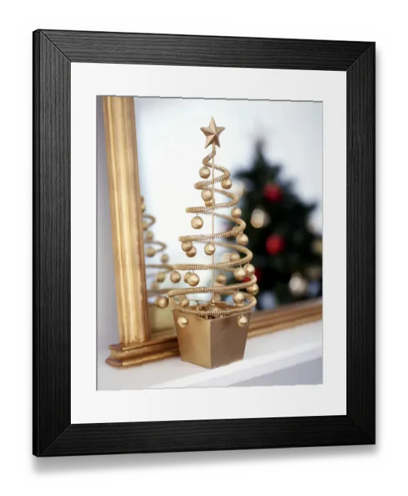 Framed Print : Small decorative, gilt abstract christmas tree on mantel shelf with real alrge green Framed Print : Small decorative, gilt abstract christmas tree on mantel shelf with real alrge green