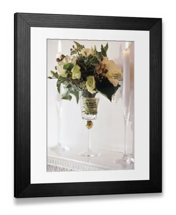 Framed Print : Arrangement of white roses and greenery in tall goblet glass between candles in tall Framed Print : Arrangement of white roses and greenery in tall goblet glass between candles in tall