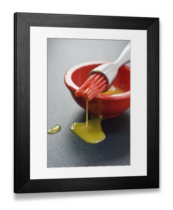 Framed Print : Egg yolk in small red bowl and dripping off red silicone bristles of modern pastry