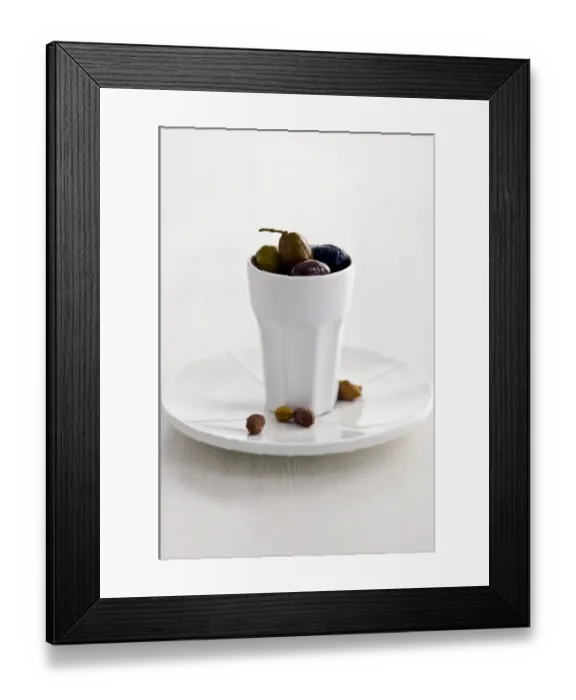 Framed Print : Mixed Italian olives in tall white ceramic pot on white plate with stones on white Framed Print : Mixed Italian olives in tall white ceramic pot on white plate with stones on white