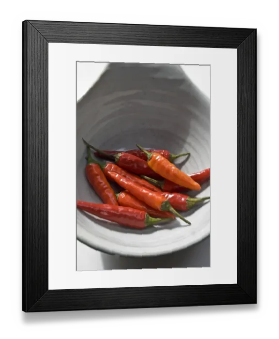 Framed Print : Small hot birds eye chilli peppers arranged on white surface. credit: Marie-Louise