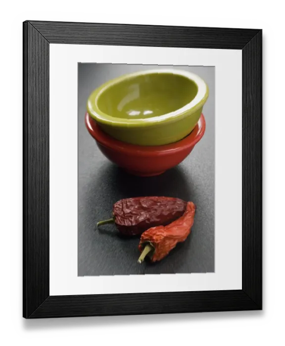 Framed Print : Two bright melamine bowls stacked on dark surface with two red hot chilli peppers Framed Print : Two bright melamine bowls stacked on dark surface with two red hot chilli peppers
