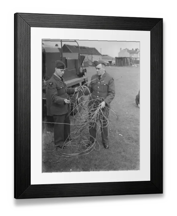Framed Print : Two men examine storm damage in the form of broken cable at a balloon barrage base