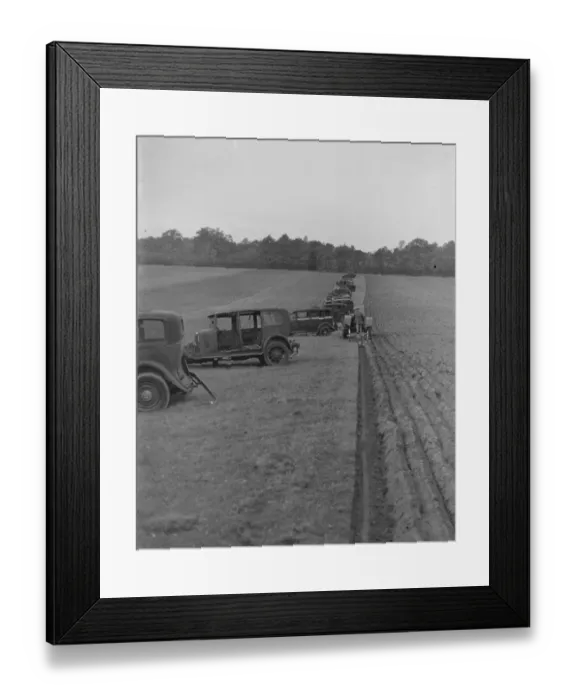 Framed Print : A farmer ploughing a field with a tractor. Alongside are old cars which have been Framed Print : A farmer ploughing a field with a tractor. Alongside are old cars which have been