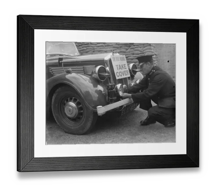 Framed Print : A policeman is fitting an air raid siren along with a warning sign to a police car