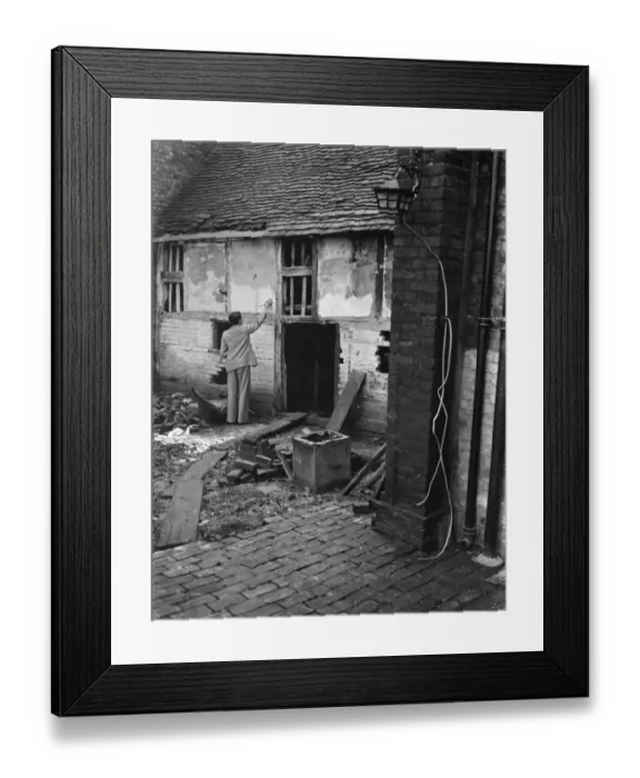 Framed Print : Mr Greenfield brushing the wall of an old dilapidated cottage to be used as a museum