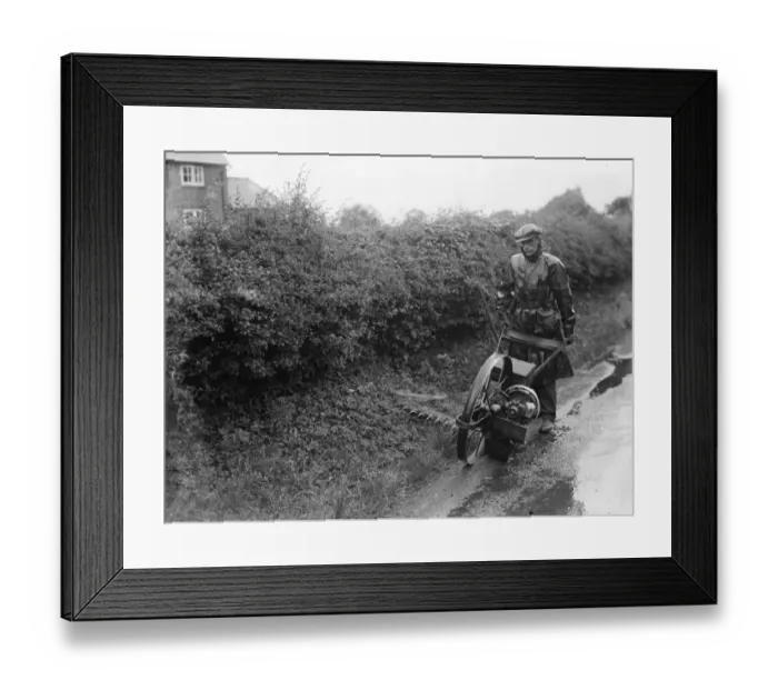 Framed Print : A maintenance man uses a motorized scythe to mow the side of the road Framed Print : A maintenance man uses a motorized scythe to mow the side of the road