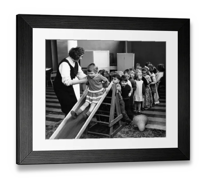 Framed Print : Mrs Joan Edison, leader of the nursery, helping her young charges on the slide Framed Print : Mrs Joan Edison, leader of the nursery, helping her young charges on the slide