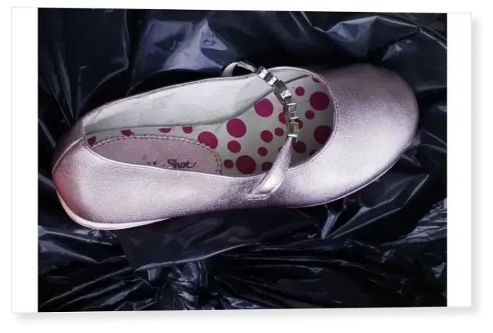Print : Girls pink party shoe discarded on top of a black bin liner Print : Girls pink party shoe discarded on top of a black bin liner