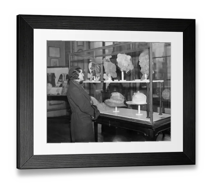 Framed Print : Girl in modern beret examines headgear of bygone days. 5 February 1935 Framed Print : Girl in modern beret examines headgear of bygone days. 5 February 1935