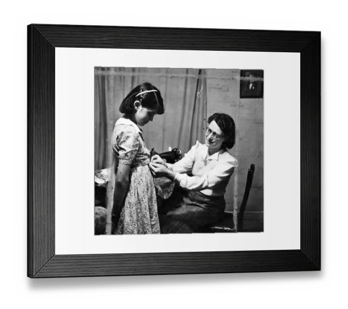 Framed Print : Woman sewing using a sewing machine and fitting a young girls dress [no caption Framed Print : Woman sewing using a sewing machine and fitting a young girls dress [no caption