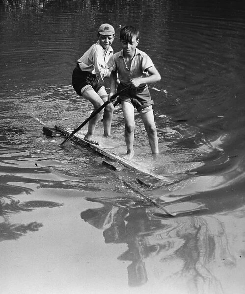Boys have good fun with an improvised raft on the village pond at Orpington, Kent