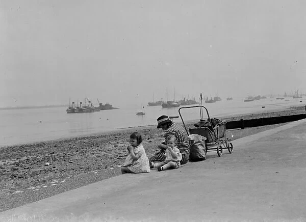 Children sit on the promenade at Gravesend river front and look out over the Thames