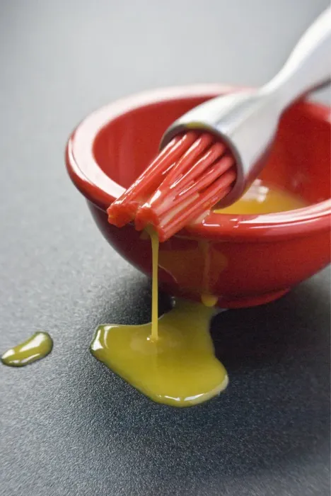 Framed Print : Egg yolk in small red bowl and dripping off red silicone bristles of modern pastry