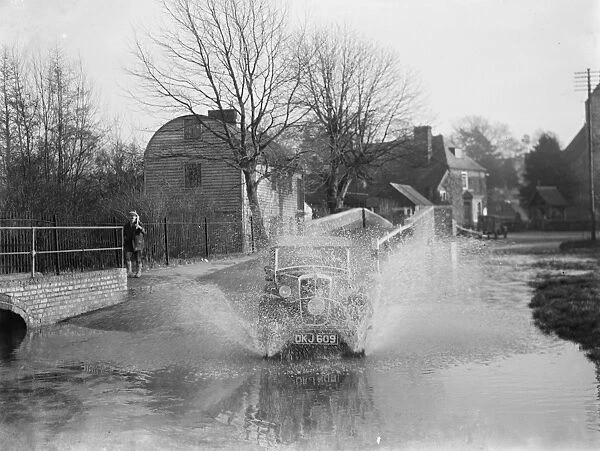 Eynsford Bridge flooded. A car ploughs through the water. 1937