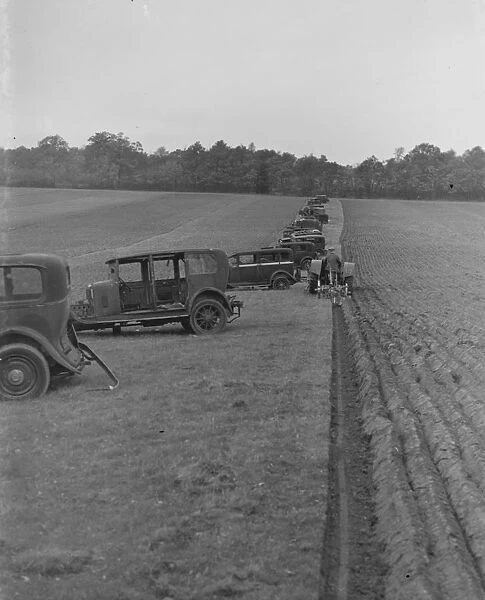 A farmer ploughing a field with a tractor. Alongside are old cars which have been