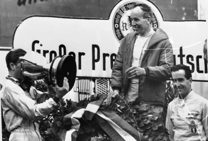 Framed Print : John Surtees looks smilingly on as Graham Hill drinks Champagne out of the Gian Cup