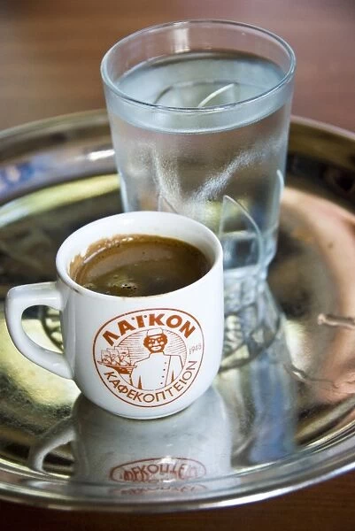 Little cup of strong Greek coffee, with glass of water on tray on table of hillside