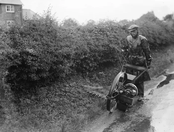 Framed Print : A maintenance man uses a motorized scythe to mow the side of the road Framed Print : A maintenance man uses a motorized scythe to mow the side of the road