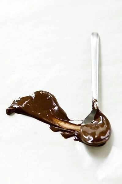 Melted chocolate smeared across white surface with a spoon leaving a plume shape