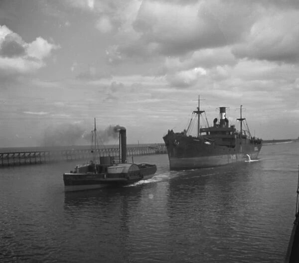 Merchant ship under tow from a paddle steamer tug. 1936